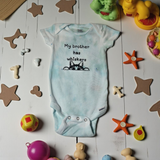 Baby onesie with text and cat illustration on a wooden floor with toys around