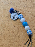 Keychain with blue, white, and checkered beads on a cork background