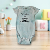 Baby onesie with 'My brother has whiskers' text on a wooden surface with a blurred background