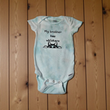 Light blue baby onesie with text and cat illustration on wooden surface