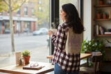 Woman holding a coffee cup in a cafe with a window view of a street.