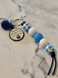 Keychain with blue and white checkered beads and a heart-shaped tag on a marble surface