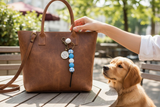 Brown leather handbag with a dog tag on a wooden table, with a dog sitting nearby.