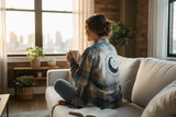 Woman sitting on a couch in a cozy living room, holding a mug and looking out a window.