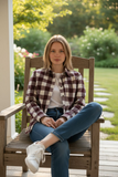 Woman sitting on a wooden chair outdoors with greenery in the background